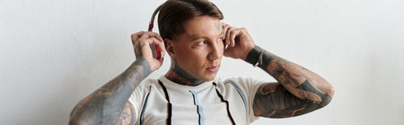 Attractive young man with tattoos adds music to his day while wearing headphones inside.の写真素材