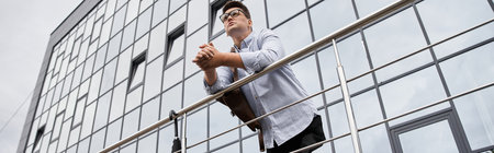 The young man stands on a balcony, looking thoughtfully at the city skyline.の写真素材
