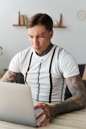 Young handsome man with tattoos works intently on his laptop at a stylish deskの写真素材