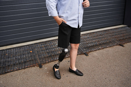 Young man stands proudly with his hands in his pockets, showcasing his prosthetic leg and outfit.の写真素材