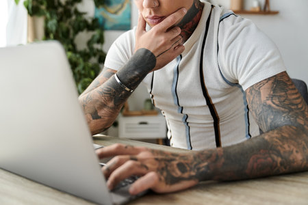 Handsome young man with tattoos is engaged in thoughtful work on a laptop at home.の写真素材