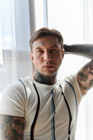 Young man with tattoos showcases his style and confidence in a well lit indoor space.の写真素材