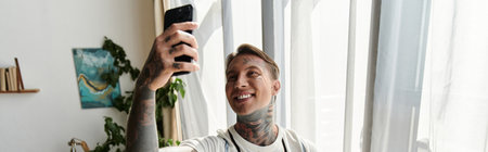 Handsome young man smiles while taking a selfie in a sunlit space surrounded by plants.の写真素材