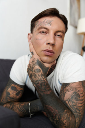 Handsome young man with tattoos sits calmly, resting his chin on his hand in a relaxed atmosphere.の写真素材