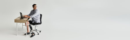 Handsome young man sits at desk, focused on laptop with a prosthetic leg visible.の写真素材