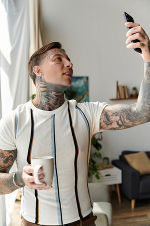 Man with tattoos takes a selfie while enjoying a drink in a modern living space.の写真素材