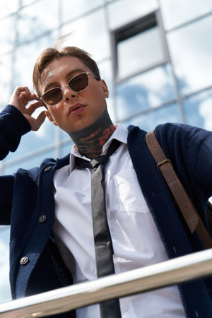 Handsome young man with tattoos adjusts his sunglasses while showcasing urban style and attitude.の写真素材