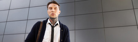 Tattooed young man in a formal outfit poses against a sleek urban backdrop.の写真素材