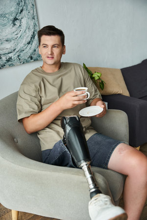 Young man enjoys a coffee and snack in a cozy living area with a prosthetic leg.の写真素材