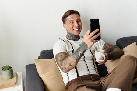 Handsome young man with tattoos enjoys his time smiling and using his smartphone while relaxed.の写真素材