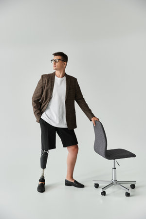 A young handsome man in a blazer stands next to a chair, showcasing his prosthetic leg.の写真素材