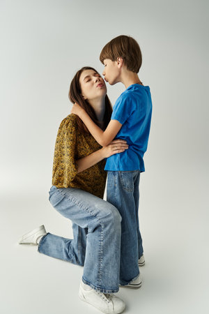 A young mother shares a tender moment with her son in casual attire while kneeling together.の写真素材
