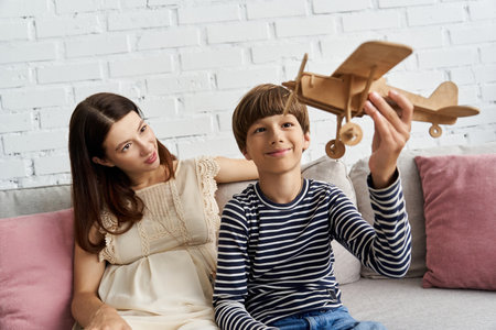 A mother and son joyfully play with a wooden toy plane in their cozy living room.の写真素材