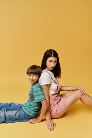 Young mother and her son sit back to back, showcasing comfort and connection in a studio.の写真素材