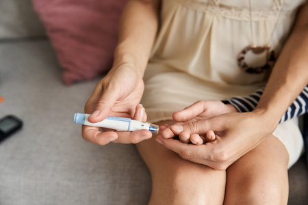 A young mother checks her son's blood sugar level in their modern living room.の写真素材