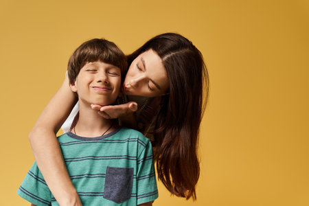 A young mother embraces her son, sharing warmth and joy in a colorful studio backdrop.の写真素材