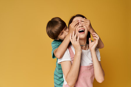 A mother shares joyful laughter with her son as he playfully covers her eyes with his hands.の写真素材