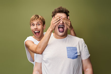 Two friends share a moment of laughter as one playfully covers the others eyes with excitement.の写真素材