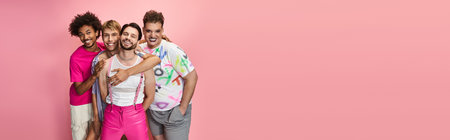 Four friends pose joyfully against a pink backdrop, showcasing their vibrant pride themed outfits.の写真素材