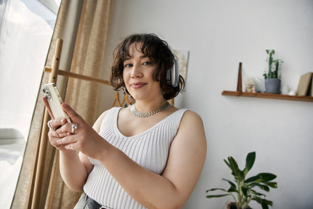 Curly-haired woman engages with her phone, radiating happiness in a modern, sunlit space.