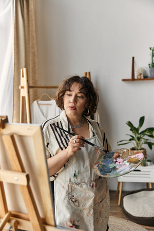 A young woman with beautiful curly hair passionately creates art in her modern apartment.の写真素材
