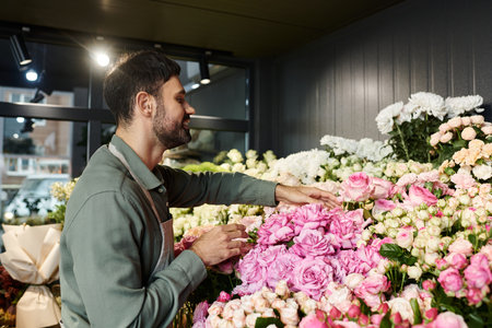 A skilled florist delicately arranges stunning pink roses among a variety of blooms in his shop.の写真素材