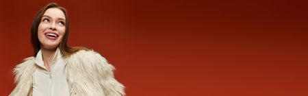 A stylish woman expresses joy against a red backdrop in fashionable attire.の写真素材