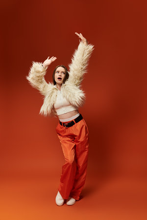 Colorful woman with a fur jacket poses with flair and energy in a vibrant orange background.の写真素材
