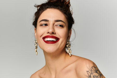 Bright smile from a young woman with a tattoo, styled hair, and stylish earrings in soft lighting.の写真素材