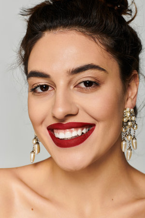 Young woman radiates beauty with striking earrings and vibrant lipstick in a studio.の写真素材