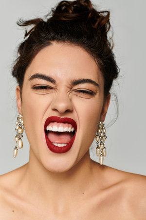 Beautiful young woman displays a joyful expression with vibrant red lipstick and elegant earrings.の写真素材