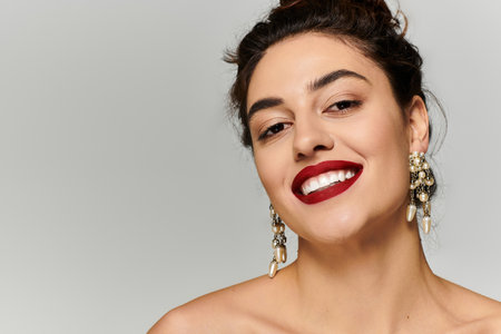 A young beautiful woman showcases a radiant smile while wearing stunning earrings and lipstick.の写真素材