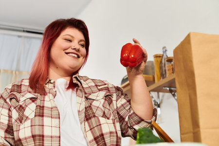 Smiling woman holds a red bell pepper, embracing her love for cooking healthy meals at home.の写真素材