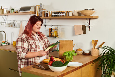 Young woman thoughtfully selects fresh vegetables while cooking in her bright kitchen space.の写真素材