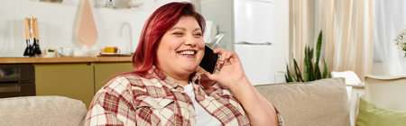 Young woman with vibrant hair laughs on the phone in a bright, inviting living room.の写真素材