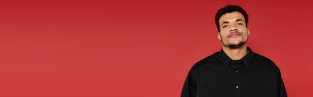 Man stands with a relaxed expression, showcasing confidence in front of a bright red backdrop.の写真素材