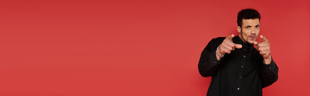 A young, handsome man playfully gestures with a confident smile by a red wall.の写真素材