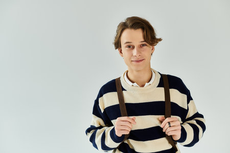 Handsome young man in a striped sweater poses confidently in a studio, representing youth culture.