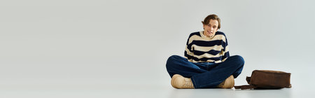 Young man in a striped sweater sits comfortably in a studio, capturing the essence of youth culture, bannerの写真素材