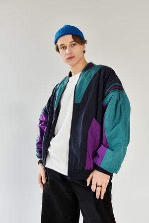 A young man in a fashionable bomber jacket stands in a studio, exuding confidence and style.