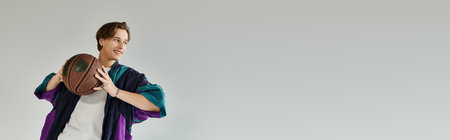 A stylish student in a bomber jacket smiles, ready to play basketball.の写真素材