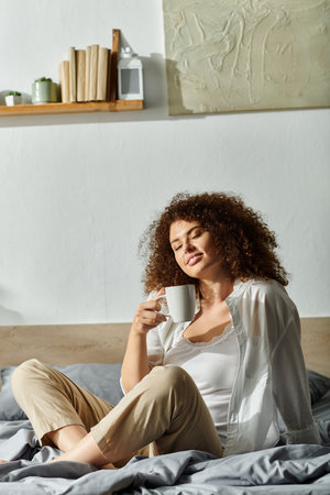 Sitting comfortably in a stylish bedroom, a woman sips coffee and unwinds.の写真素材