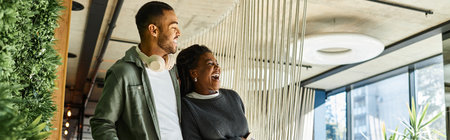 A cheerful young couple laughs together while exploring a stylish hotel lobby during their vacation.