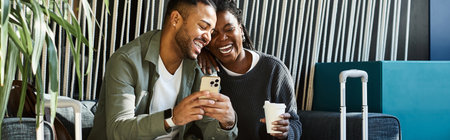A happy young African American couple shares laughter while checking their travel plans in a hotel lobby.の写真素材