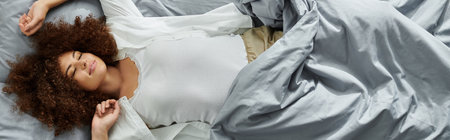 The woman relaxes peacefully in bed, surrounded by soft bedding.の写真素材