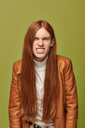 Young man with long red hair shows strong emotions while dressed in a stylish leather outfit.の写真素材