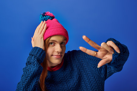 Young man with long red hair poses playfully in a colorful beanie, showing vibrant emotions.の写真素材