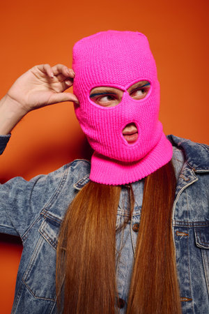 Young man expresses deep emotions while wearing a bright pink mask against an orange backdrop.の写真素材