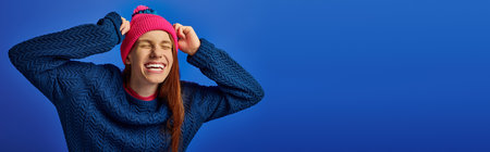 Joyful young man beams with happiness, showcasing his long red hair and vibrant beanie.