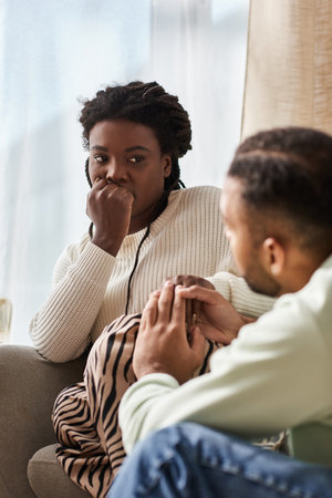 African American man holding hand of his worried girlfriend in their cozy living roomの写真素材